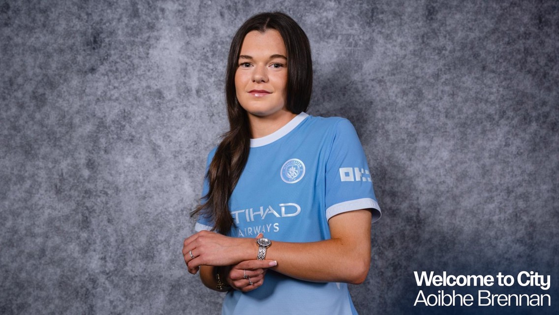 A woman wearing a Manchester City jersey stands against a gray background, with text reading 'Welcome to City Aoibhe Brennan.'