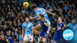 Soccer players in action with one jumping to head the ball. 'Official Verdict' badge in bottom right.