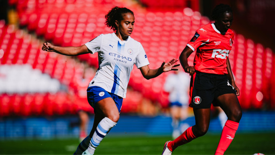Two women soccer players in motion. One in a white Manchester City kit and the other in a red Charlton Athletic kit. They are playing in a stadium with red seats.