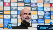 A manager at a press conference with a backdrop featuring various sponsor logos such as Puma and Asahi Super Dry.