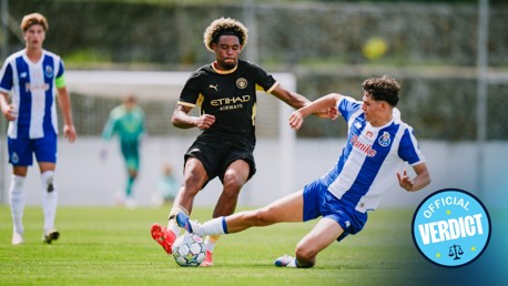 Two soccer players from opposing teams compete for the ball during a match. One player attempts to tackle the other, who is wearing a Manchester City kit.