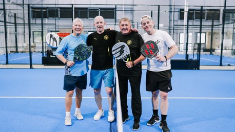 Four men holding padel rackets pose on a blue padel court.