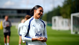 A woman in a Manchester City training outfit is smiling on a football field during a training session.