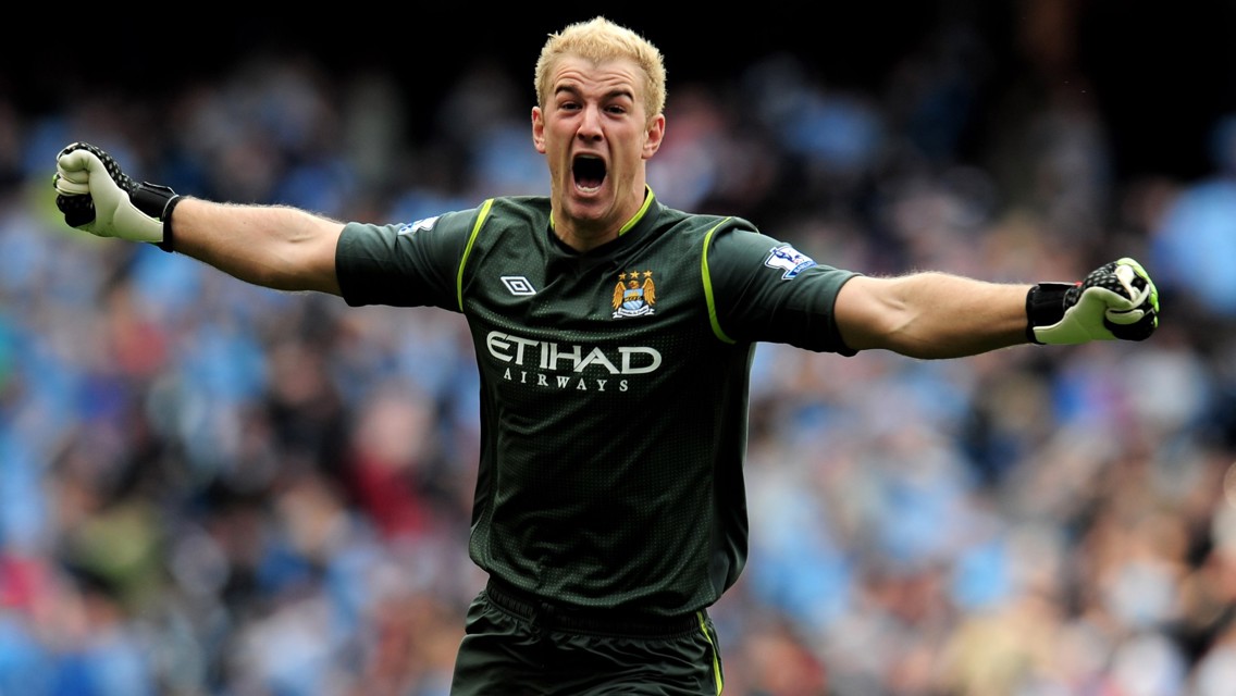 A goalkeeper wearing a Manchester City kit with arms outstretched, on a football field.
