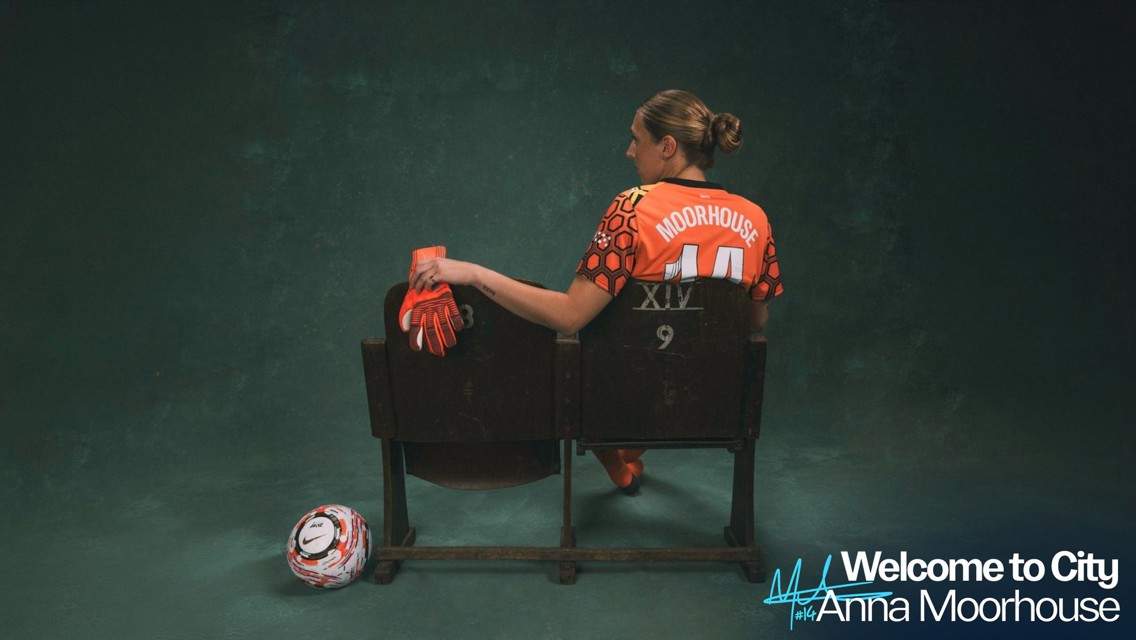 A football player wearing an orange goalkeeper kit with 'Moorhouse' and '14' on the back, sitting on a seat with gloves and a ball nearby. Text reads 'Welcome to City Anna Moorhouse'.