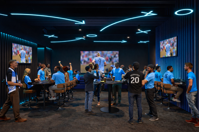 Group of people wearing blue and black jerseys watching a soccer match in a bar with screens displaying the game.