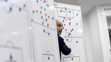 A person strategizing on football tactics with magnetic markers on a whiteboard in a sports setting.