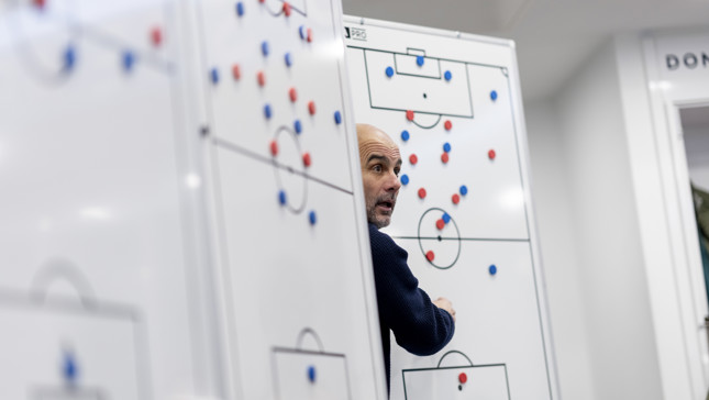 A person strategizing on football tactics with magnetic markers on a whiteboard in a sports setting.