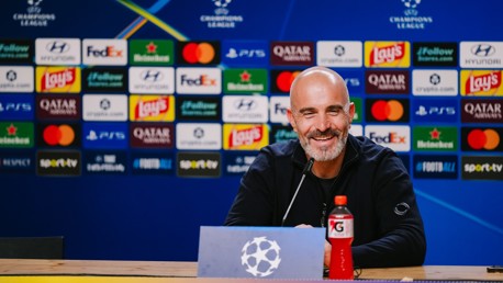 A man seated at a table during a UEFA Champions League press conference with a background of sponsor logos.