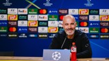 A man seated at a table during a UEFA Champions League press conference with a background of sponsor logos.
