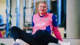 A person wearing a Manchester City training tracksuit in pink and blue is sitting on the floor with one leg extended.