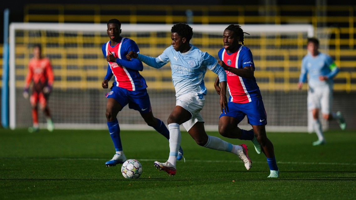 Soccer match between Manchester City and Paris Saint-Germain. Players are in action on a field, wearing blue and red uniforms. The ball is in play.