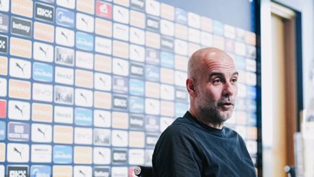 A person with a blurred face sits in front of a backdrop featuring various logos and sponsors associated with Manchester City.