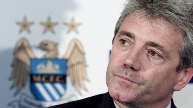Person at a press conference with a Manchester City crest visible in the background.