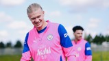 Dos personas vistiendo el uniforme de entrenamiento del Manchester City, en colores rosa y azul, están al aire libre durante una sesión de entrenamiento.