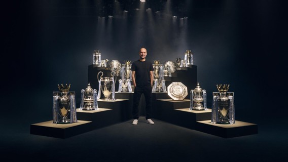 A person standing among various football trophies on platforms with dramatic lighting.