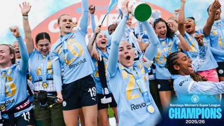 Football team wearing light blue jerseys with 'Revolut' sponsor celebrating with a trophy. Barclays Women's Super League 2025/26 Champions text visible.