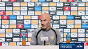 A man at a Manchester City press conference sits in front of a wall filled with various sponsor logos.