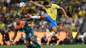 A soccer player in a yellow jersey jumps to kick the ball while another player in a multicolored jersey tries to defend during a match.