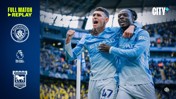 Two Manchester City players celebrating during a match at Etihad Stadium. The left side shows logos and text promoting a match replay against Ipswich Town.