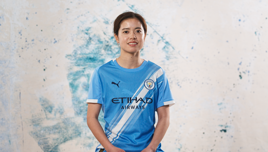 Person wearing a Manchester City football jersey with Puma and Etihad Airways logos on it against a textured background.