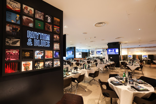 A dining area with neatly arranged tables. On one wall, there's a display featuring 'Rhythm & Blues' surrounded by album covers.