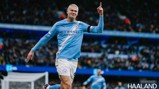 A football player in a Manchester City jersey celebrates a goal with a raised finger gesture. The text '200 appearances' and 'Haaland' are visible.