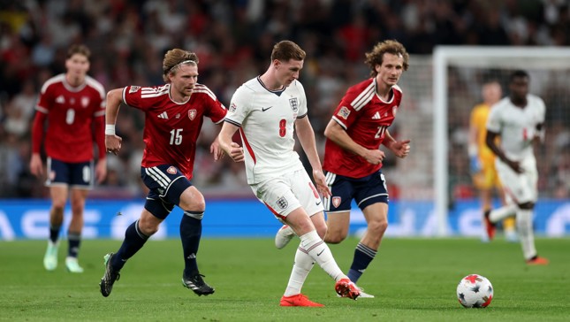 Soccer players from England and Czech Republic in action during a match, focusing on a player in a white jersey controlling the ball, pursued by players in red jerseys.