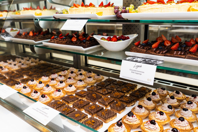 A variety of desserts displayed on a glass shelf, including chocolate brownies with toppings and assorted pastries.