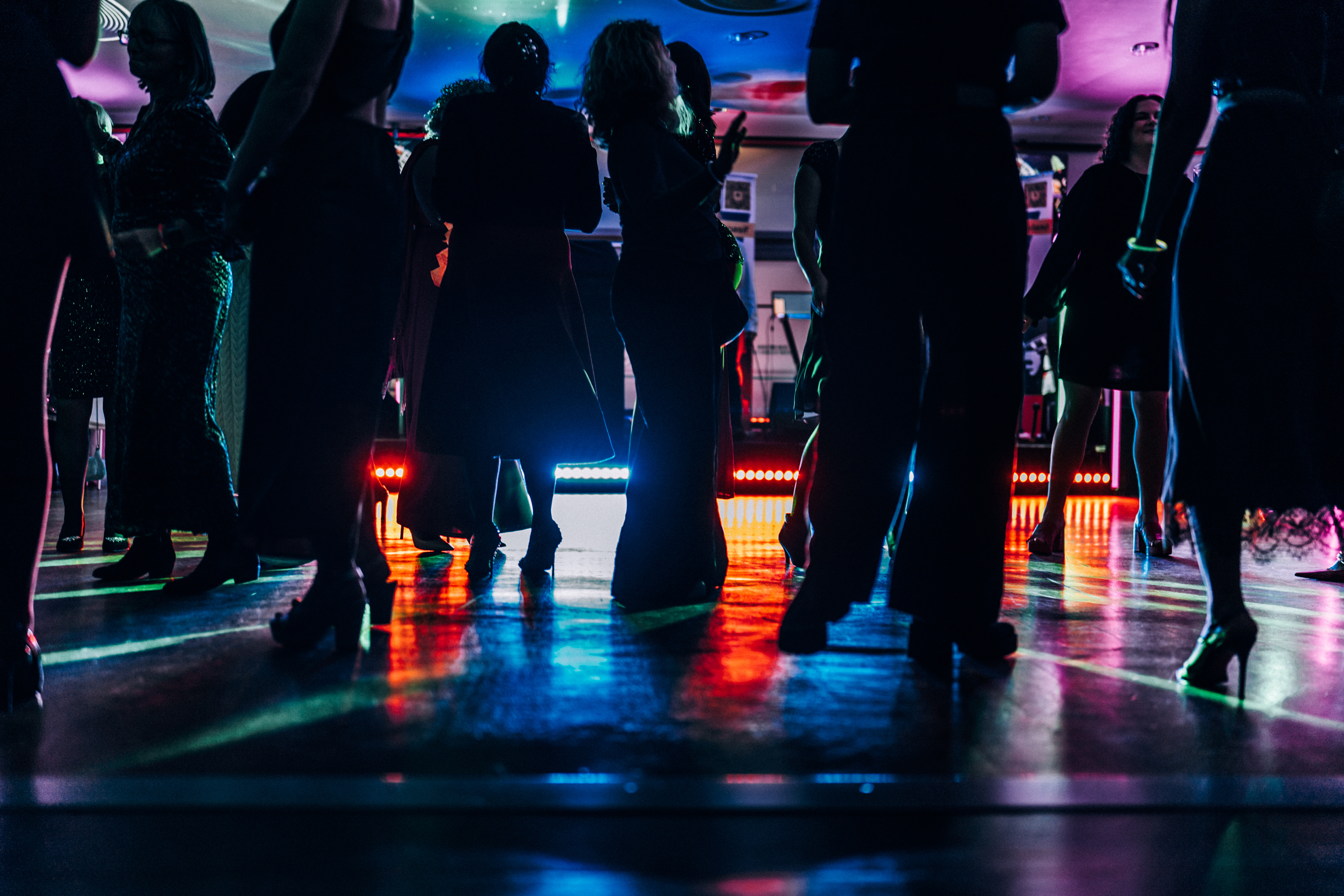 Silhouetted people dancing on a colorful, illuminated dance floor at a party or event.