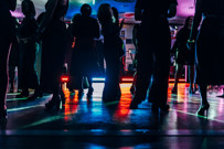 Silhouetted people dancing on a colorful, illuminated dance floor at a party or event.