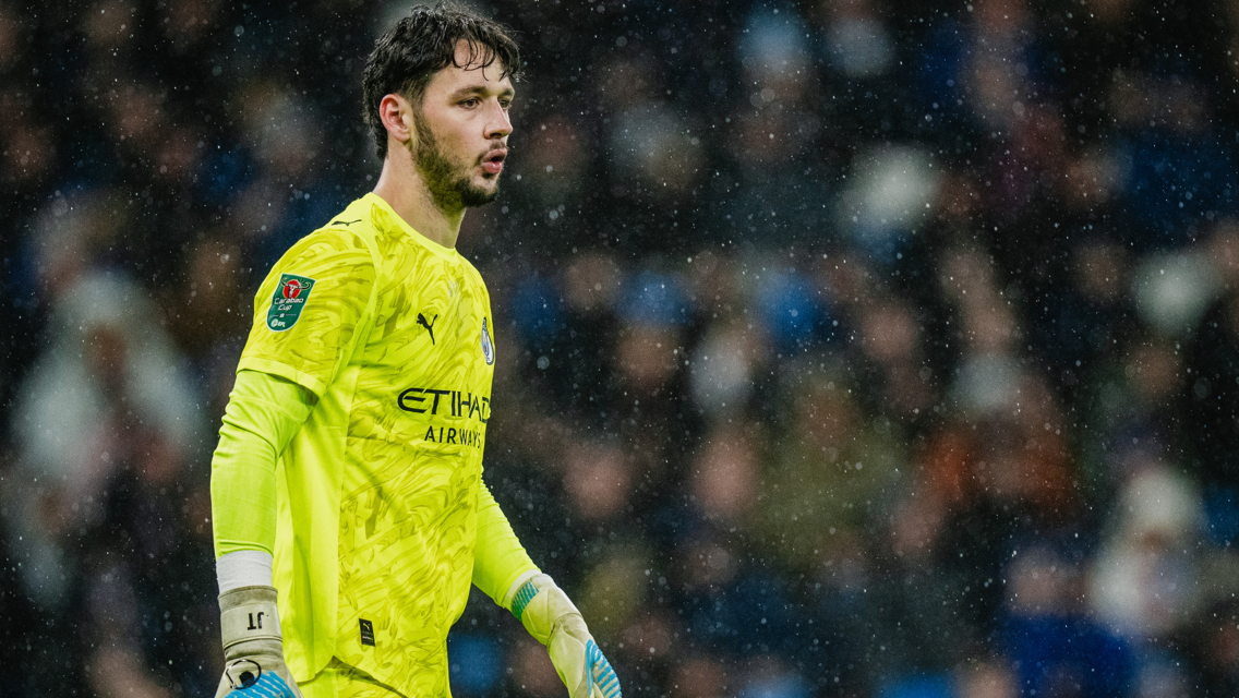 A football player wearing a yellow Manchester City goalkeeper kit during a match. The Etihad Airways sponsor logo is visible on the shirt.