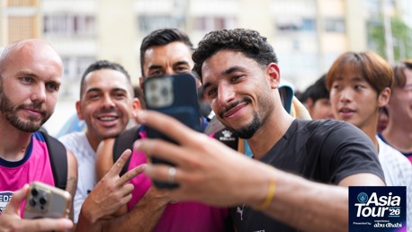 A group of people taking a selfie, wearing Manchester City shirts. The scene is part of Manchester City's Asia Tour '26.