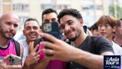 A group of people taking a selfie, wearing Manchester City shirts. The scene is part of Manchester City's Asia Tour '26.