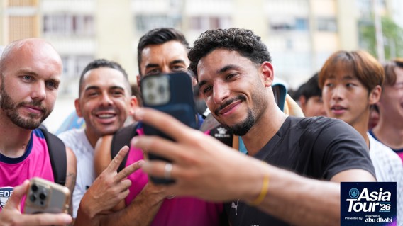 A group of people taking a selfie, wearing Manchester City shirts. The scene is part of Manchester City's Asia Tour '26.