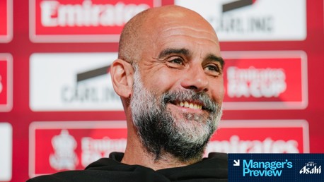 A press conference setting with a blurred person in focus. The background features logos and text for the Emirates FA Cup. The image includes text indicating 'Manager's Preview' and 'Asahi'.