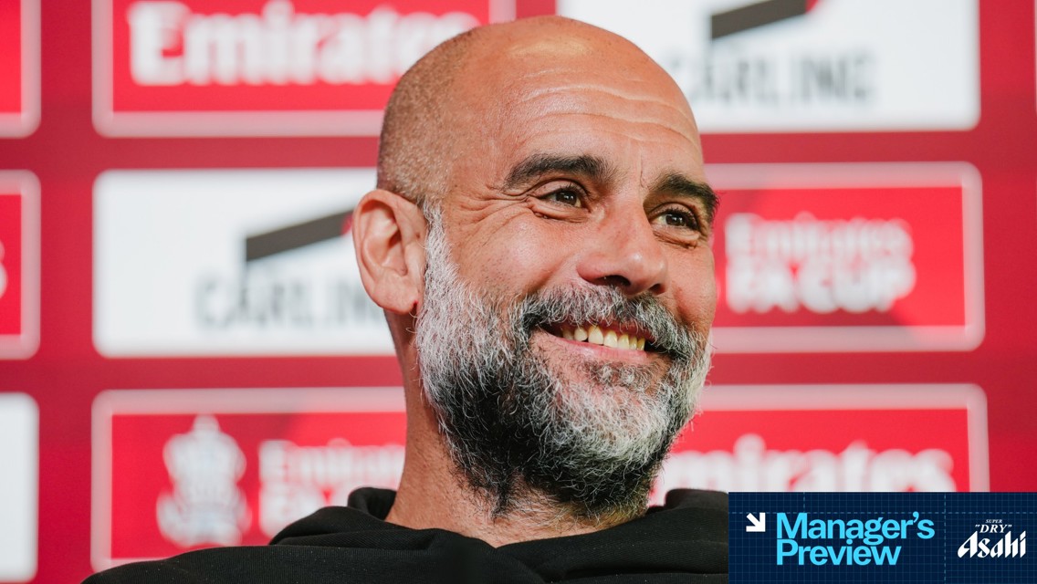 A press conference setting with a blurred person in focus. The background features logos and text for the Emirates FA Cup. The image includes text indicating 'Manager's Preview' and 'Asahi'.