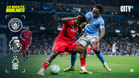 A Manchester City player in a light blue jersey and a Nottingham Forest player in a red jersey are engaged in a physical battle for the ball during a Premier League match. The stadium is filled with spectators.