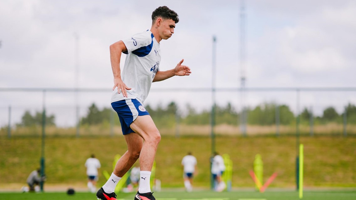 A person in a Manchester City training outfit running on a football field during practice.
