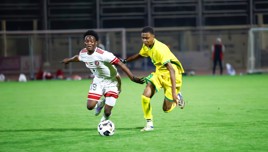 Two soccer players in mid-action: one in a white kit and the other in yellow, competing for the ball on a grass field.
