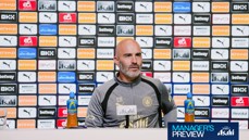 A person in a Manchester City tracksuit sits at a press conference table with branding logos behind them, including Puma and Etihad. There are Lucozade bottles on the table.