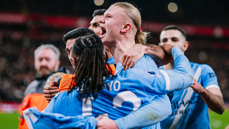 Manchester City players wearing blue jerseys are in a team huddle celebrating on the field after a match.