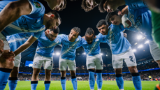 Manchester City players in a huddle on the field at night with stadium lights illuminating the scene.