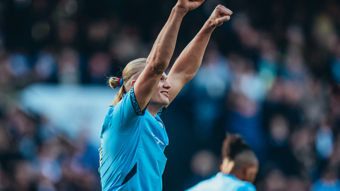 A player in a blue jersey with a blurred face raising both arms in celebration during a match.