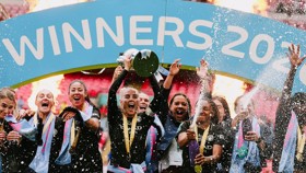Soccer team celebrating victory under 'Winners 2023' banner with fireworks and champagne shower.
