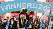 Soccer team celebrating victory under 'Winners 2023' banner with fireworks and champagne shower.