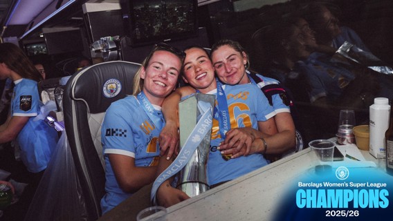 Manchester City Women's team members celebrate their Barclays Women's Super League 2025/26 championship on a bus. They hold a trophy and wear their team jerseys.