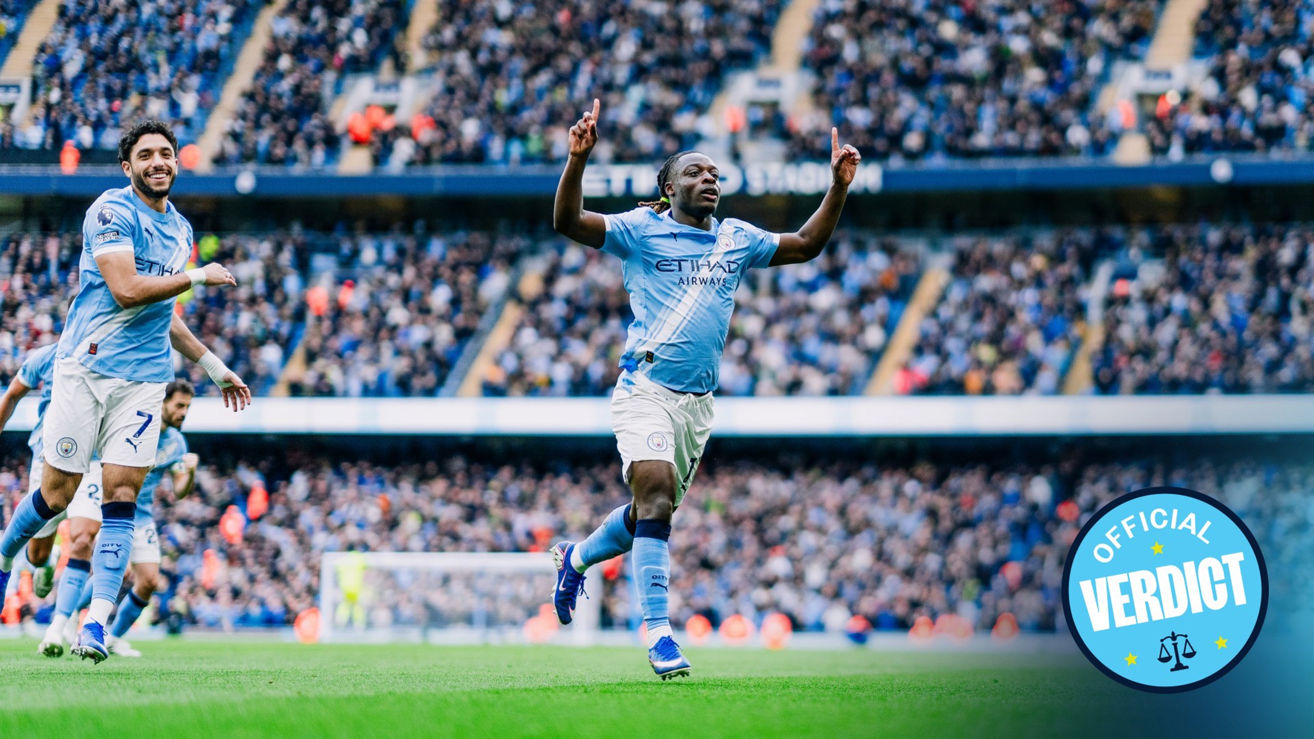 Manchester City players celebrating a goal at Etihad Stadium. A blue badge reading 'Official Verdict' is visible.