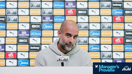 A person speaking at a press conference in front of a backdrop featuring various logos including Puma, Etihad, and Asahi. A microphone with Asahi branding is visible.