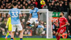 Players from Manchester City and Liverpool compete for the ball during a soccer match. A Manchester City player is jumping to head the ball.